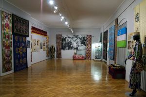 Fragment ekspozycji - ogólny widok na salę (widoczne gabloty, manekiny w strojach z Uzbekistanu, na ścianach barwne tkaniny...