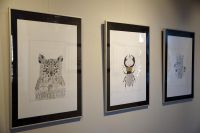 Prace artystki wiszące na ścianie, przedstawiające połączenie architektury i zwierząt