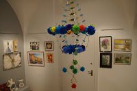 Fragment ekspozycji - na pierwszym planie "pająk" z bibuły i słomy, w tle obrazy, hafty, maskotki