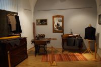 Fragment ekspozycji - m.in. komoda z materiałami, maszyna do szycia, lustro, manekin krawiecki