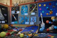 Fragment ekspozycji, duża ilość prac dzieci przedstawiających: kosmos, planety, rakietę Perun